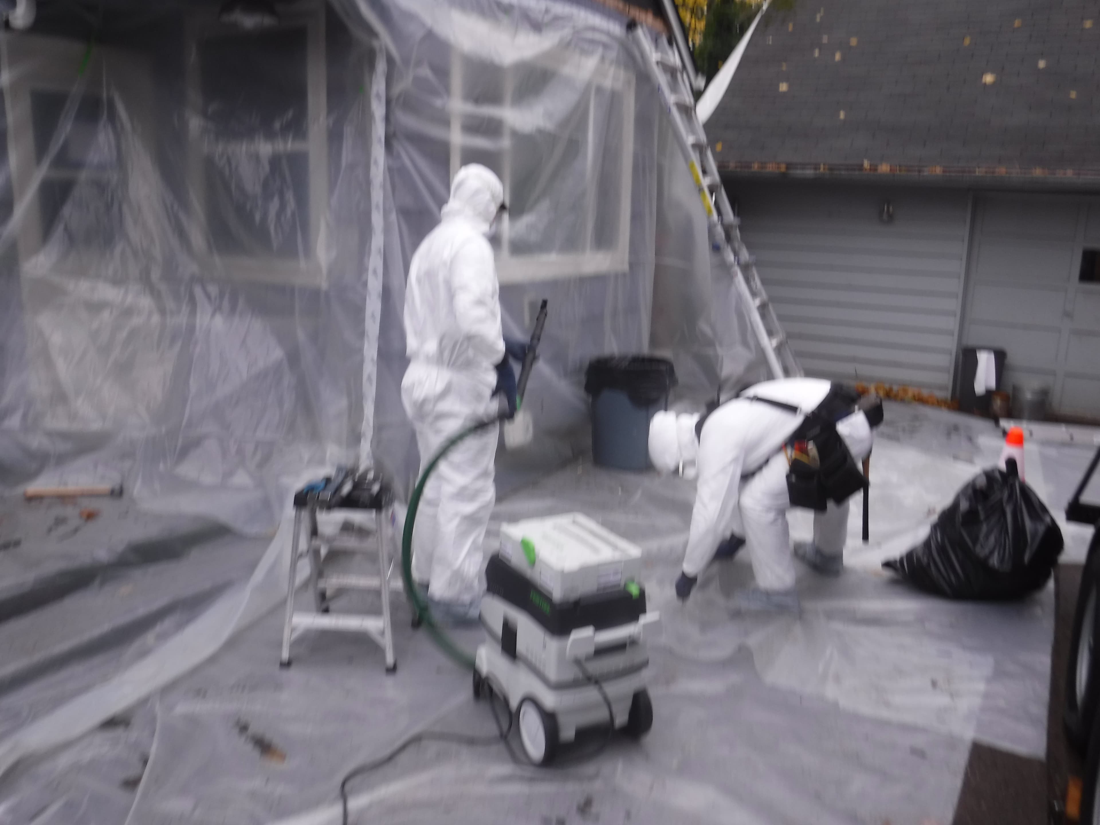 Lead abatement worker in protective suit setting up containment barriers